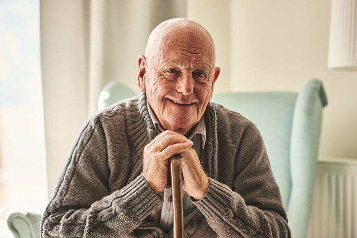 A senior man sitting down with his walking stick, smiling.